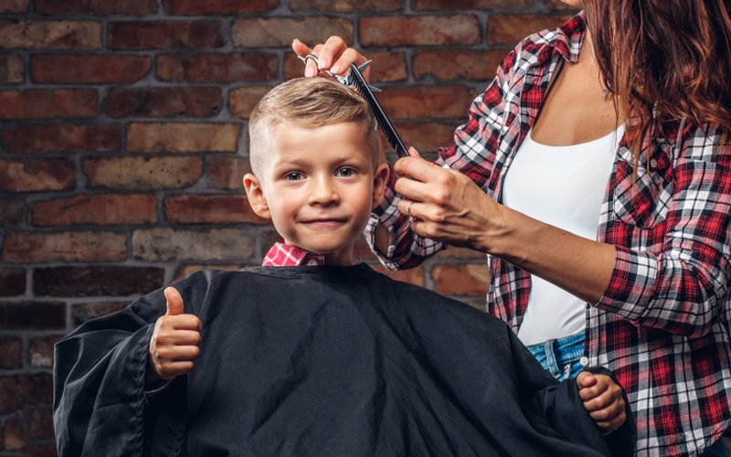 Kleine jongen die een kapsel krijgt van een meisje in een effen shirt en open wit onderhemd