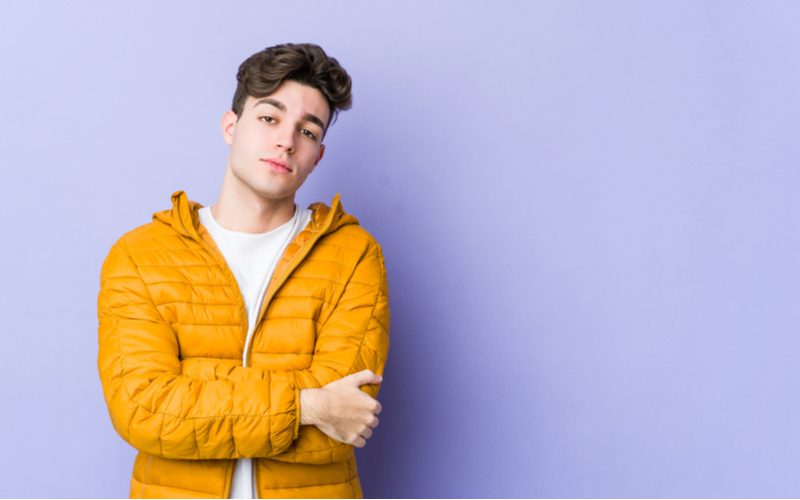 Long-Top Taper With Feathered Fringe op een man in een oranje pufferjack die met zijn armen over elkaar staat in een paarse kamer.