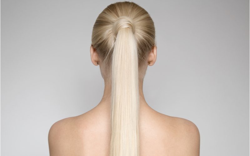 Vrouw zonder shirt kijkt weg van de camera met een Elegant Wrapped Ponytail die tot halverwege haar rug hangt.