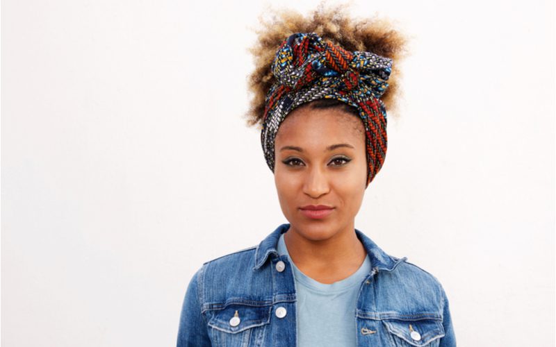 Tied Scarf Updo (een gemakkelijk kapsel) op een Afro-Amerikaanse vrouw in een spijkerjasje in een witte kamer.