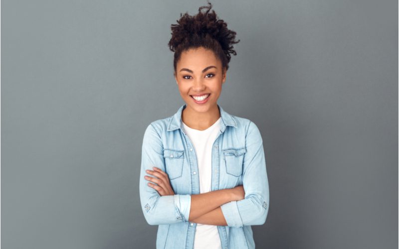 High Puff Pony weergegeven op een zwarte vrouw die haar armen kruist in een spijkerjasje in een studio voor een stuk over gemakkelijke kapsels.