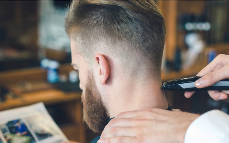 Slicked-Back Low Bald Fade op een man die zijn decolleté laat opfrissen door een kapper die buiten beeld is.