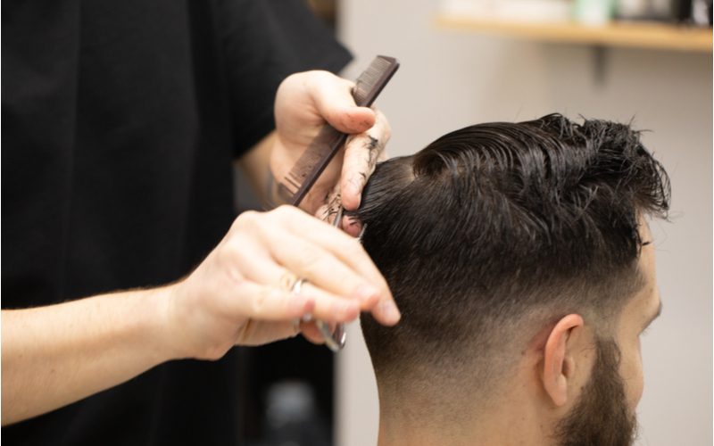 Man krijgt een lage daling huid fade kapsel met een rommelige top van een kapper in een zwart shirt wiens gezicht het uit het frame