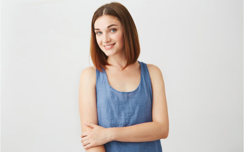 Vrouw met een lang tot halflang kapsel en een blauw denim shirt zonder mouwen die een arm vasthoudt.