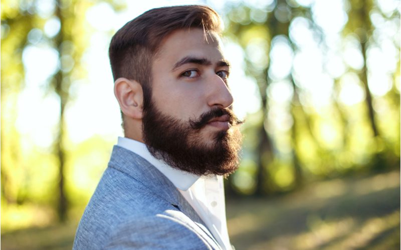 Dapper Comb Over Burst Fade gedragen door een man in een blauwgrijze blazer met wit overhemd.