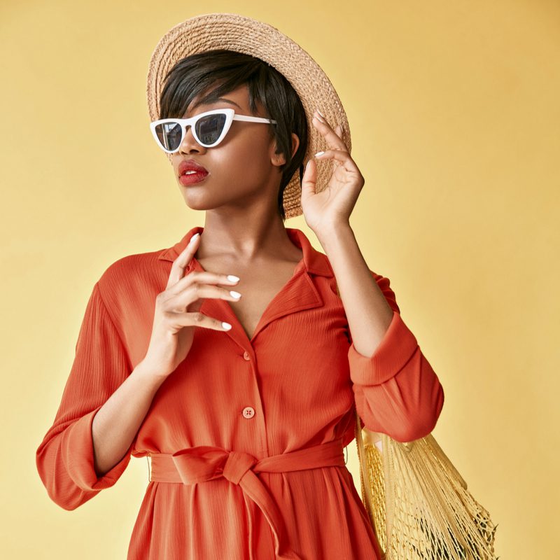 Choppy Textured Black Bob Kapsel op een Afro-Amerikaanse vrouw met een toeristische hoed en een rode jurk.