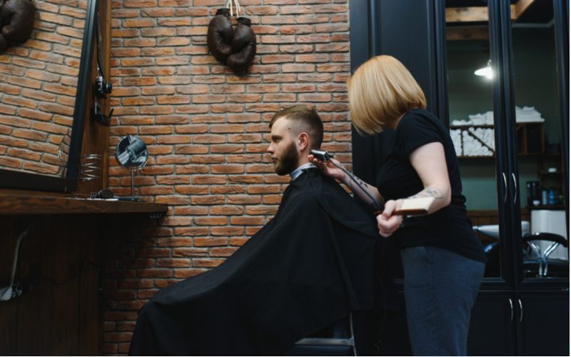 Vrouwelijke kapper geeft een man een mohawk fade kapsel terwijl hij een zwarte cape draagt