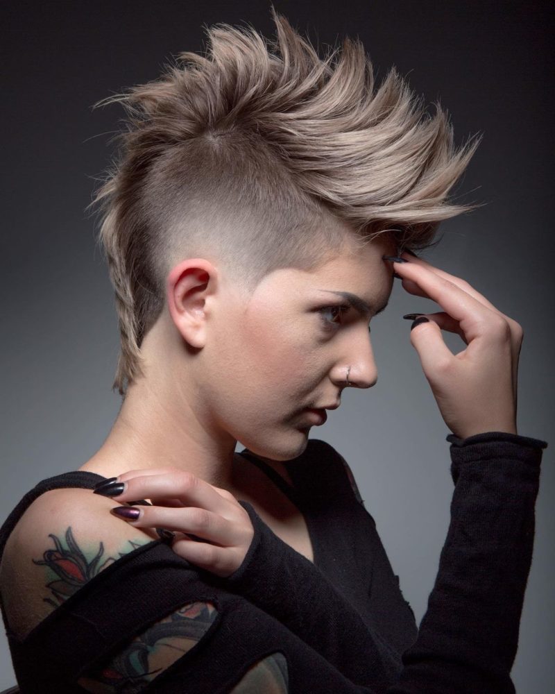 Vrouw met een vrouwelijke mohawk met spikes die haar voorhoofd vasthoudt.