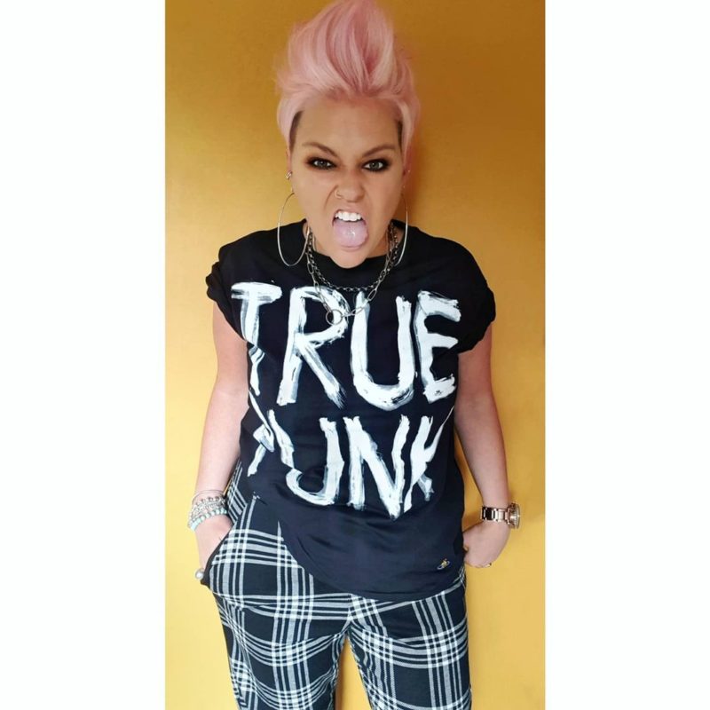 Vrouw met een roze vrouwelijke mohawk in een echt punk shirt met chucks en geruite broek