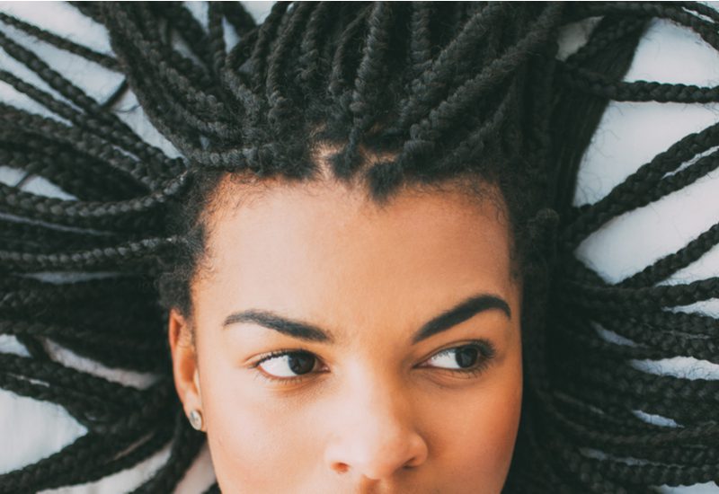 Natural Box Braids voor een roundup op tribal braid kapsels op een vrouw die op haar rug ligt en omhoog kijkt.