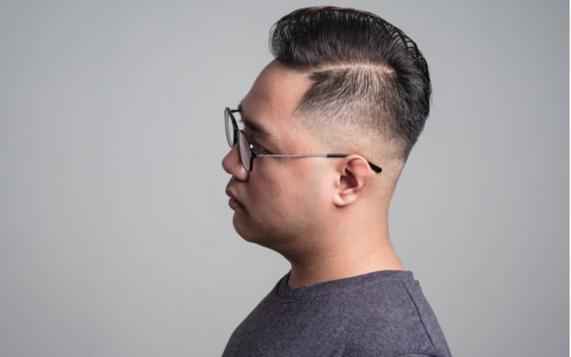 Man met een Comb-Over Low Fade kapsel in een zijprofiel foto met een hard gedeelte aan de linkerkant van zijn hoofd.