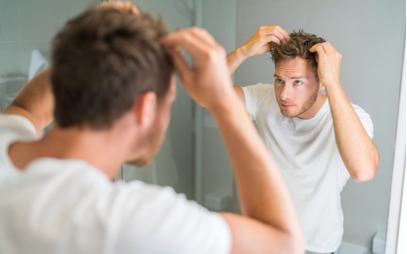 Een man stylt een faux havik terwijl hij in de badkamerspiegel kijkt en de spikes op zijn hoofd aanraakt.