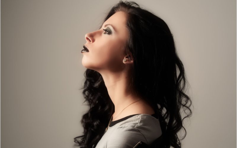 Vrouw met een ravengolf punk kapsel draagt bordeauxrode lippenstift en kijkt omhoog