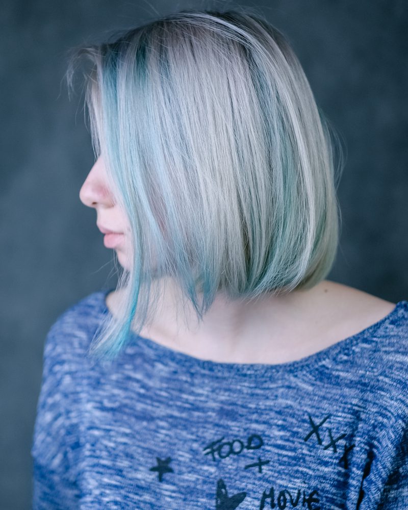 Choppy lange blonde bob kapsel met lowlights op een vrouw in een fancy blauw shirt