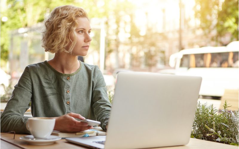 Vrouw met een warrige kinlengte bob zittend in een stoel buiten een coffeeshop