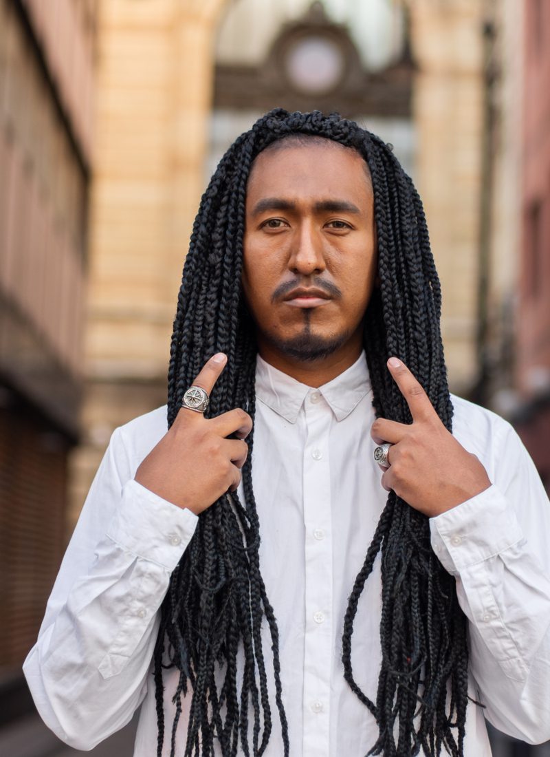 Man schommelt box braids voor mannen in een wit hemd en staat met beide zijden van zijn haar in de hand