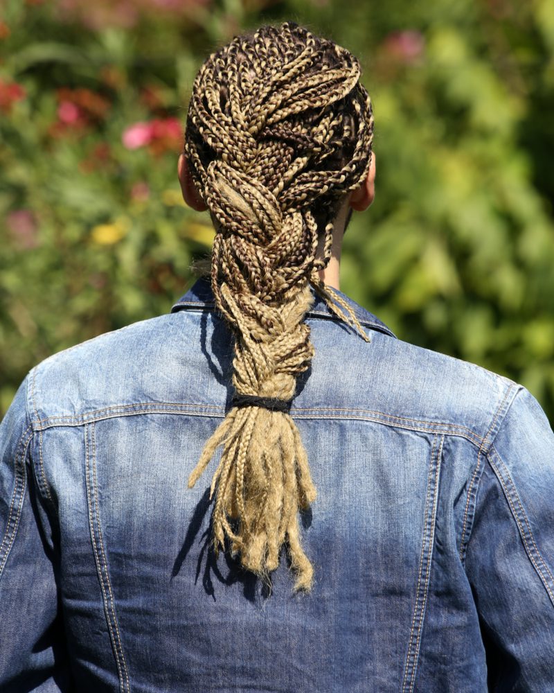 Gevlochten doosvlechten voor mannen op een kerel in een jeansjasje die naar een bos bomen kijkt