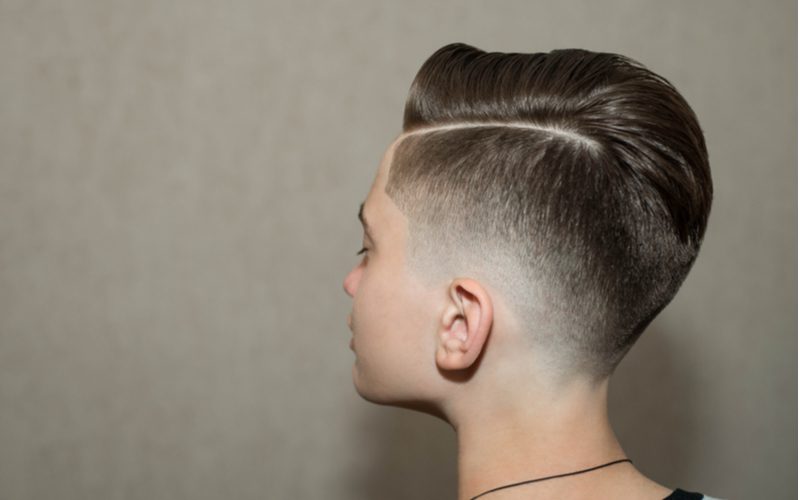 Jonge tienerjongen met een retro undercut fade kapsel staat in een grijze studio en kijkt naar links