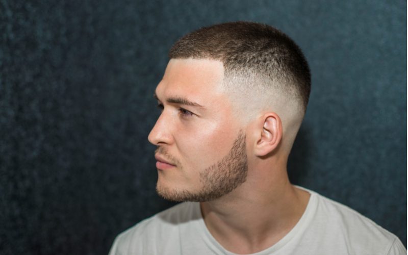 Man met een gezoete undercut fade kijkt voor zich uit in een wit t-shirt in een zwarte kamer