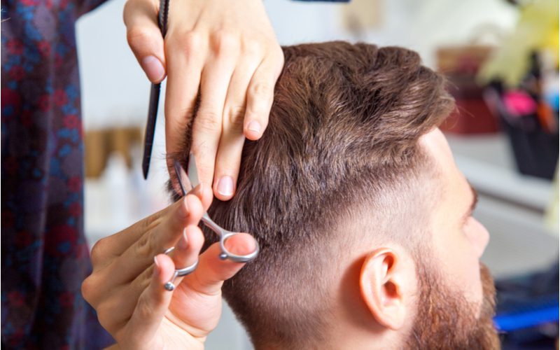 Man in de stoel van een stylist krijgt een low fade undercut met een schaar en een kam