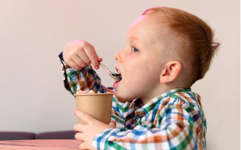 Jonge jongen met een vierkante undercut fade eet cheerios uit een beker in een geruit gekleurd shirt