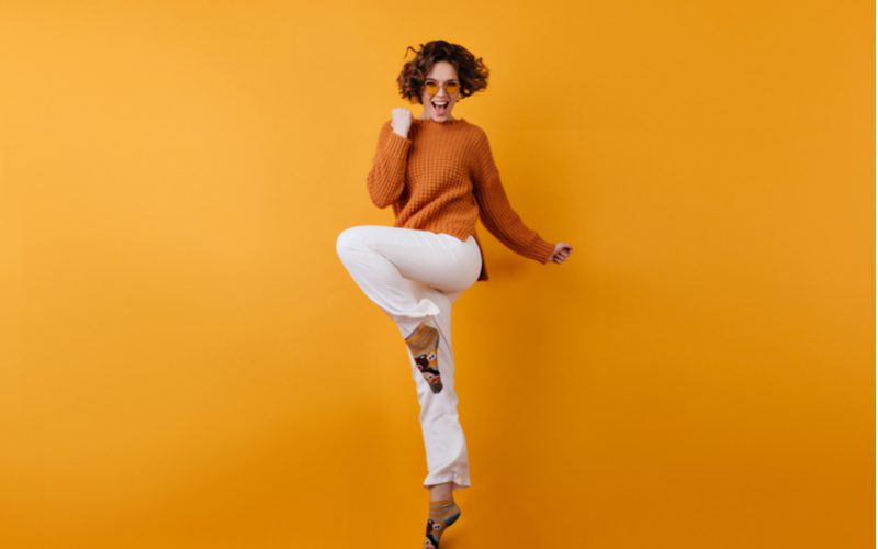 Kort bobkapsel in de vorm van een paddestoel op een vrouw in een oranje trui en witte broek