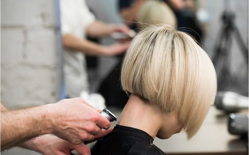 Inverted Blonde Bob op een vrouw in een salonstoel die haar decolleté geschoren krijgt.