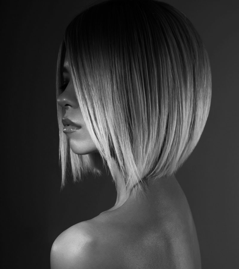 Vrouw met een blond midi inverted bob kapsel staat in een donkere kamer voor een zwart-wit opname