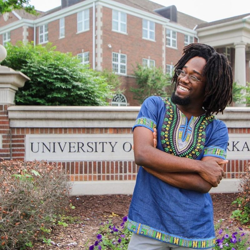 Man staat voor de Universiteit van Centraal Arkansas met vrije vorm dreads in een traditioneel Afrikaans overhemd.