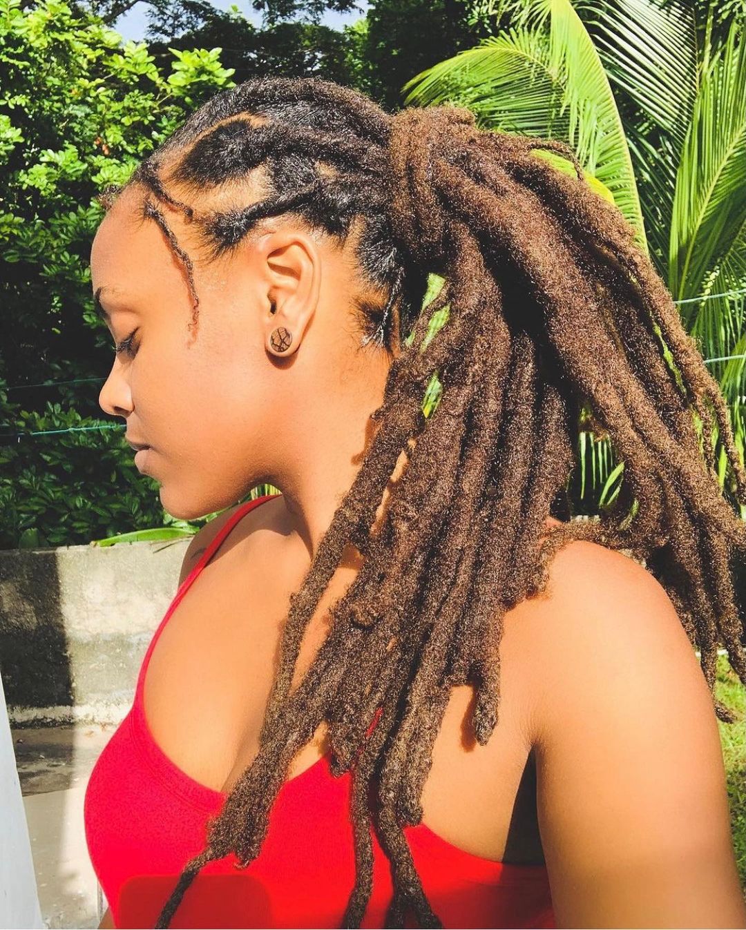 Vrouw in een rood shirt draagt freeform locs en kijkt naar rechts.