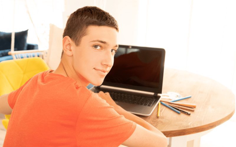 Short Crop op een jongen in een oranje shirt voor een laptop voor een stuk over jongenskapsels