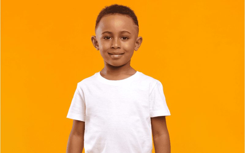 High Fade With Shaved Line op een jongen in een wit shirt in een oranje kamer