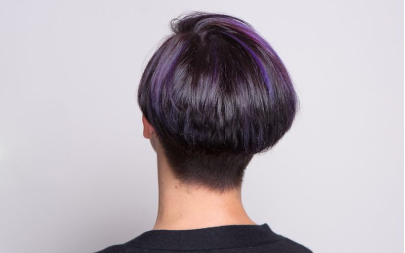 Modern paddestoel bob kapsel met paarse haarstrepen op een vrouw die naar een muur kijkt