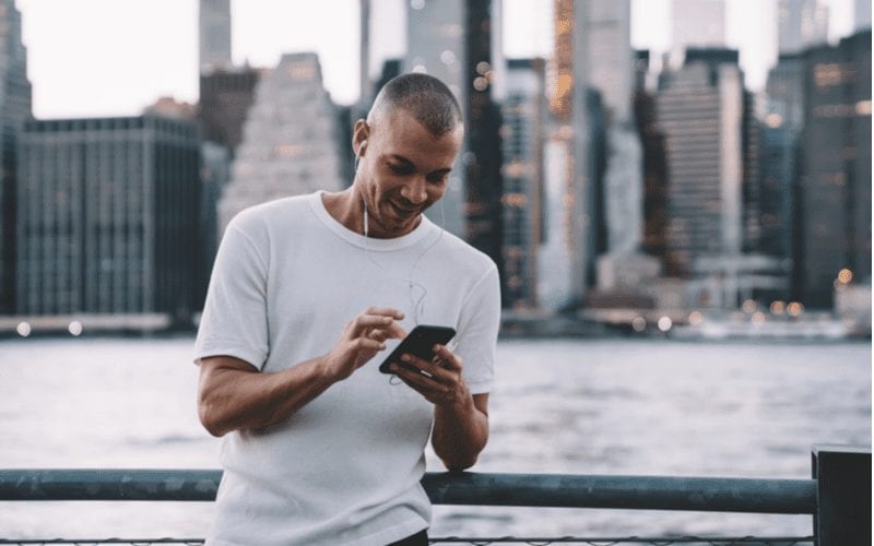 Widow's Peak Skin Fade op een man in een wit shirt met ronde hals die naar een telefoon kijkt voor een skyline.