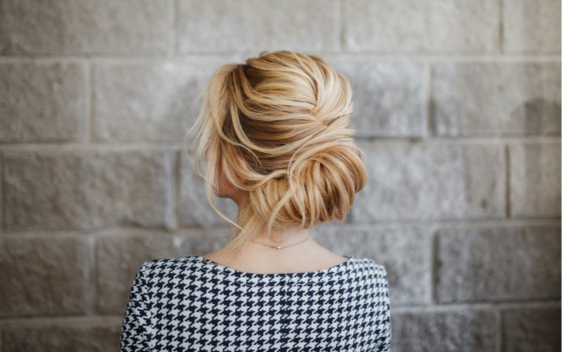 Vrouw met een lage twist knot, een geweldig moeder van de bruidegom kapsel, draagt een zwart-wit gedessineerde blouse en kijkt naar een bakstenen muur.