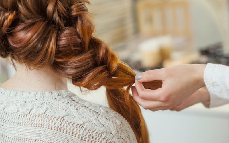 Enkele gevlochten moeder van de bruidegom kapsel wordt gestyled door een gezichtsloze vrouw in wat lijkt op een woonkamer