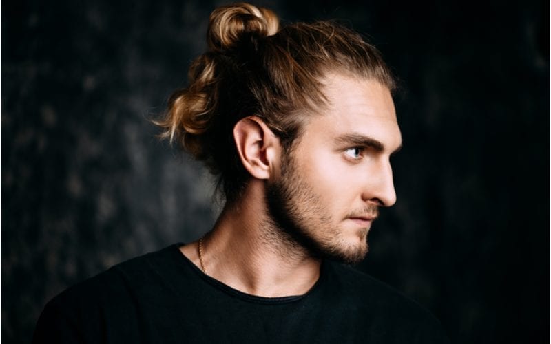 Man met een lange man bun opgestoken in zijn haar kijkt serieus naar links in een verduisterde kamer