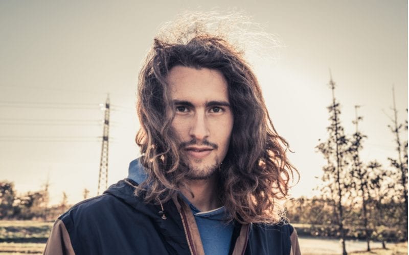 Man in een park met een hoogspanningslijn op de achtergrond laat zijn lange haar wapperen in de wind voor een stuk over lange kapsels voor mannen