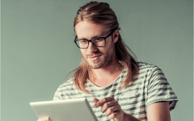 Man met half opgestoken haar kijkt op een tablet met bril voor een bos lange kapsels voor mannen