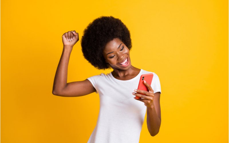 Gal met een traditionele jaren '70 afro die een telefoon vasthoudt en juicht met haar hand boven haar hoofd.