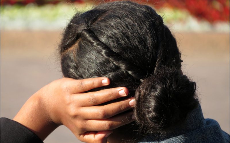 Low Bun With a Twist op een zwarte vrouw die buiten op een bankje zit.