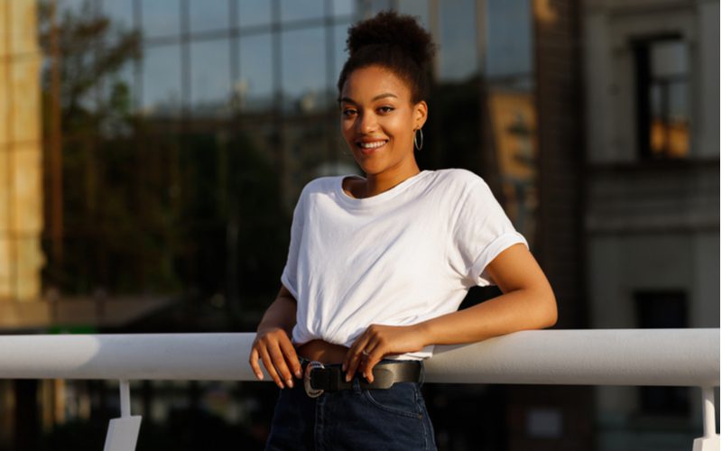 Vrouw draagt een wit t-shirt en donkere jeans leunt tegen een railing