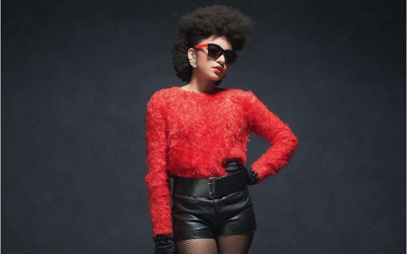 Zwarte vrouw met een geplukte afro in een rood shirt en een zwarte leren broek.