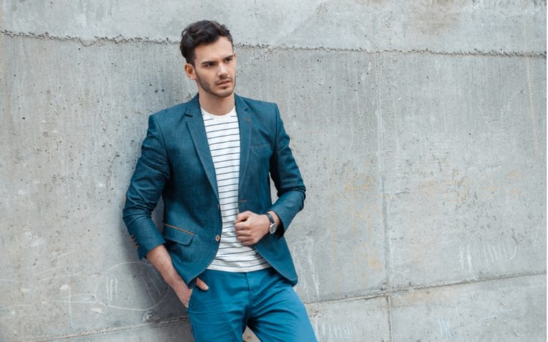 Man in groene broek en een korte groenblauwe blazer leunt tegen een betonnen muur schommelen een kapsel voor golvend haar mannen