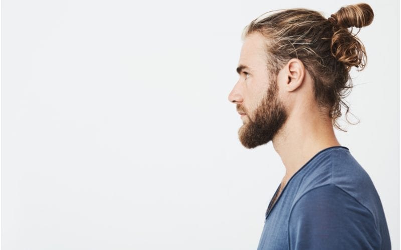 Zijprofiel van een golvend haar man in een blauw overhemd staand in een studio op een witte achtergrond