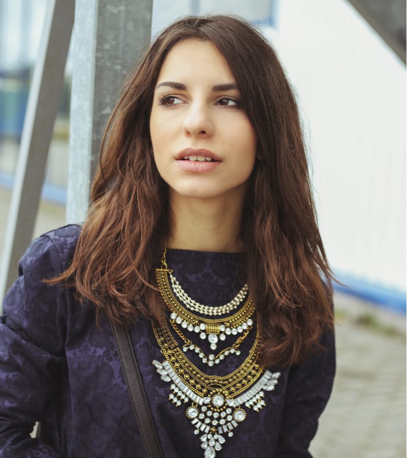 Euro-looking gal in een dikke kralenketting kijkt naar rechts en loopt door de straat.