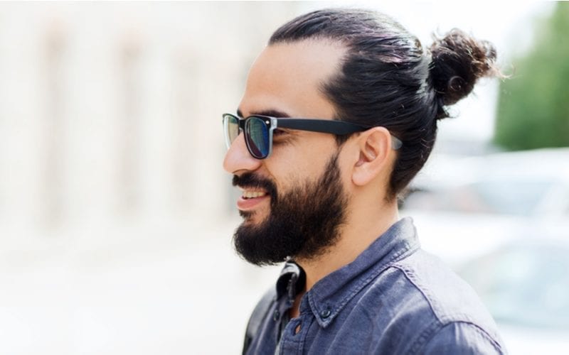 Man met donkere zonnebril met een baard en een man bun heeft een van onze favoriete kapsels voor mannen met ronde gezichten