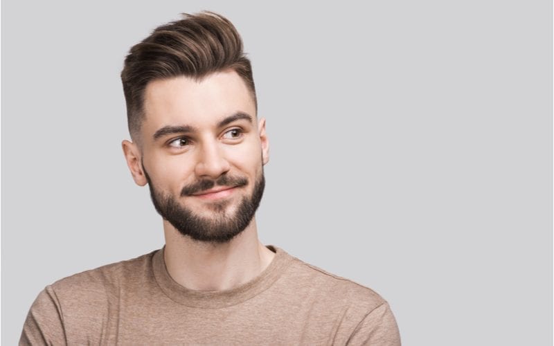 Man in een shirt met lange mouwen en een nonchalant pompadour kapsel kijkt naar links zonder te glimlachen.