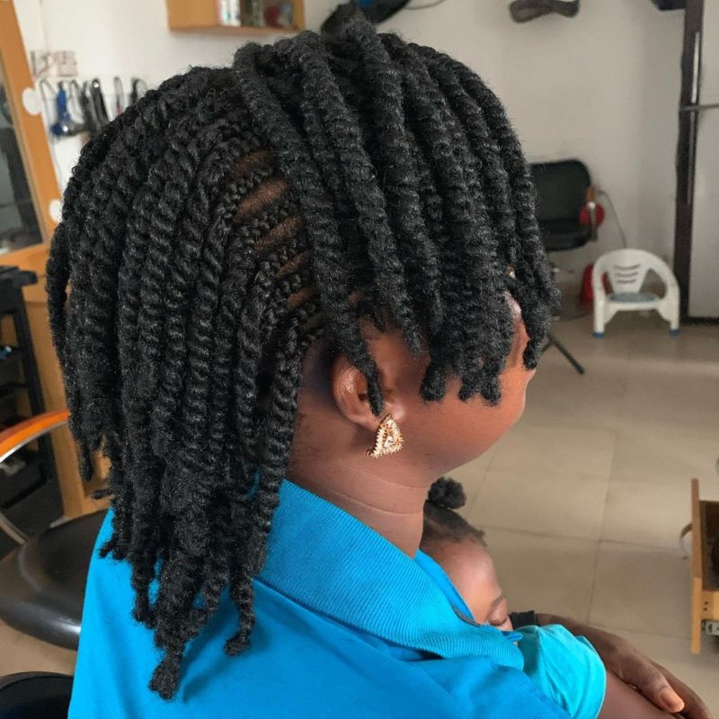 Mooie vrouw met natuurlijke kinky twists die ook erg dik zijn zit in een salonstoel en houdt een baby vast.