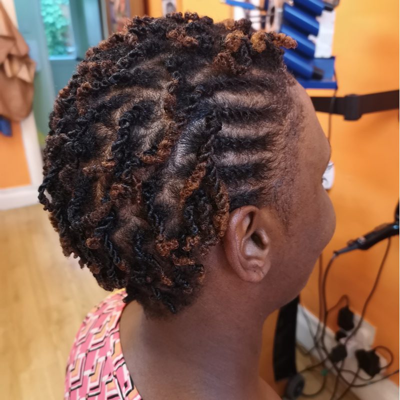 Zwarte vrouw met micro kinky twists zit in een vlecht salon te glimlachen